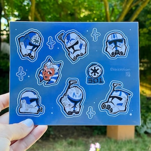 May include: A set of blue and white Star Wars clone trooper stickers on a blue background with white stars. The stickers feature the characters Captain Rex, Ahsoka Tano, and other clone troopers. The text "301" and "Blackseafoam" are also included on the stickers.