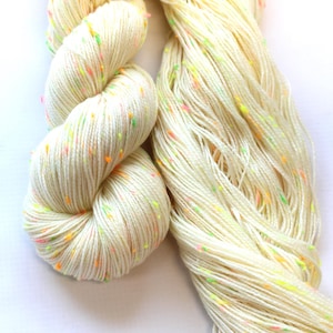 May include: Two skeins of cream-colored yarn with flecks of neon green, pink, and orange.