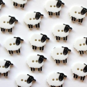 May include: A collection of white sheep-shaped buttons with black faces, legs, and ears. Each button has two small holes for sewing. The buttons are scattered across a white surface.