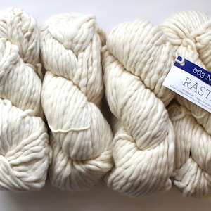 May include: Three skeins of white yarn, labeled "RASTA 063 NATURAL" with a blue and white label. The yarn is thick and fluffy, perfect for knitting or crocheting.
