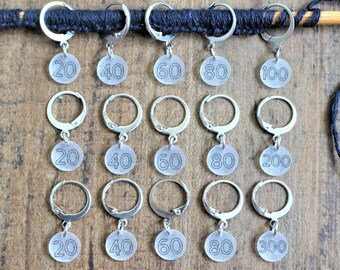 May include: A set of 15 silver stitch markers with clear plastic beads. The beads are numbered 20, 40, 60, 80, 100, 200, and 300. The markers are strung on a black yarn.