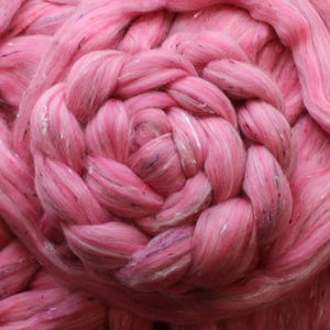 May include: Close-up of pink roving wool, arranged in a circular pattern. The wool has a soft texture with subtle flecks of color throughout. The fibers are tightly spun, suggesting a high-quality material for fiber art projects.