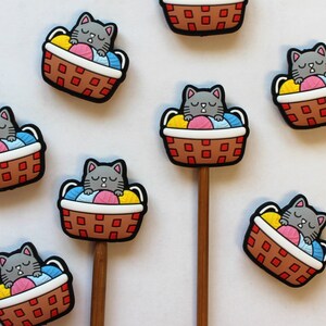 May include: Set of ten gray cat sleeping in a basket charms with colorful yarn balls. The charms are attached to wooden sticks.