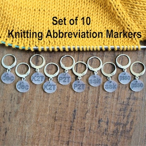 May include: Set of 10 knitting abbreviation markers. The markers are silver with clear plastic discs that have knitting abbreviations printed on them. The abbreviations include: dec, K2T, P2T, ssk, psso.