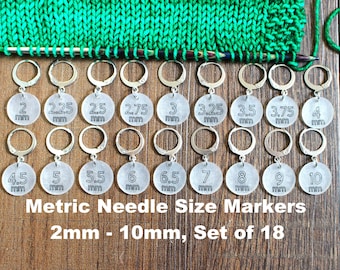 May include: Set of 18 silver knitting needle size markers, with numbers 2mm to 10mm printed on each marker. The markers are arranged in two rows on a wooden surface.