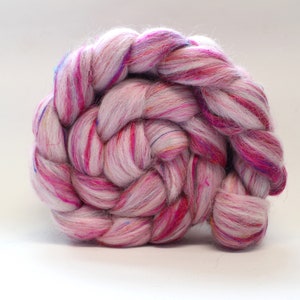 Puede incluir: Primer plano de un paquete de vell&oacute;n de lana rosa, blanco y azul trenzado. El vell&oacute;n est&aacute; dispuesto en espiral.