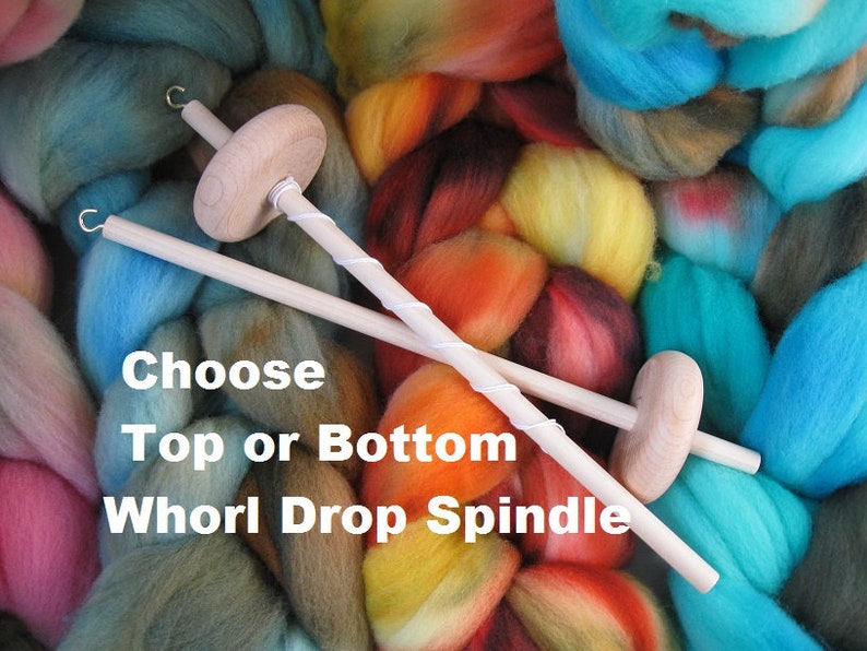 May include: Two wooden drop spindles with a whorl on each end. The spindles are crossed over each other. The spindles are surrounded by colorful yarn. The text "Choose Top or Bottom Whorl Drop Spindle" is written below the spindles.