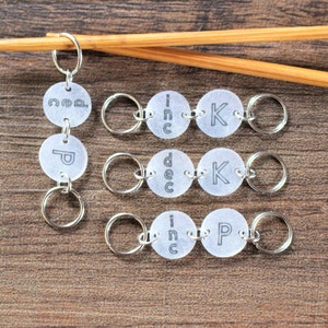 May include: Set of six silver knitting stitch markers with clear plastic discs. The discs have the words "inc", "dec", "k", "p", "co", and "inc" printed on them.