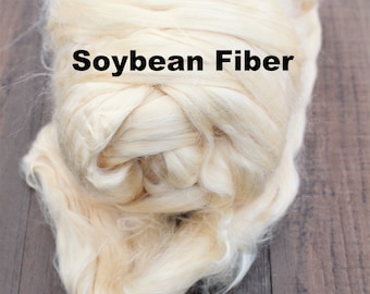 May include: A close-up of a clump of off-white soybean fiber. The fiber is soft and fluffy, and it is arranged in a loose, tangled mass. The text "Soybean Fiber" is printed in black letters on the fiber.
