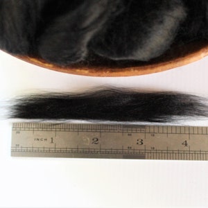 May include: A close-up of a black wool fiber sample measured against a ruler. The fiber is approximately 4 inches long.