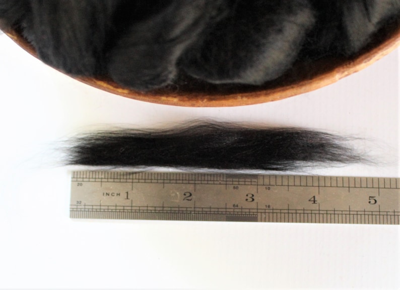 May include: A close-up of a black wool fiber sample measured against a ruler. The fiber is approximately 4 inches long.