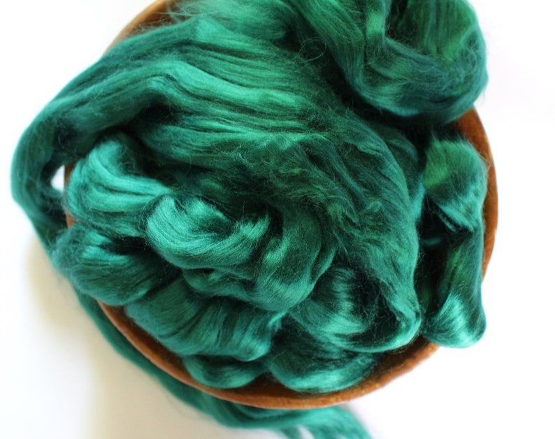 May include: A bowl filled with emerald green silk fiber. The fiber is soft and fluffy, and it is perfect for spinning or felting.