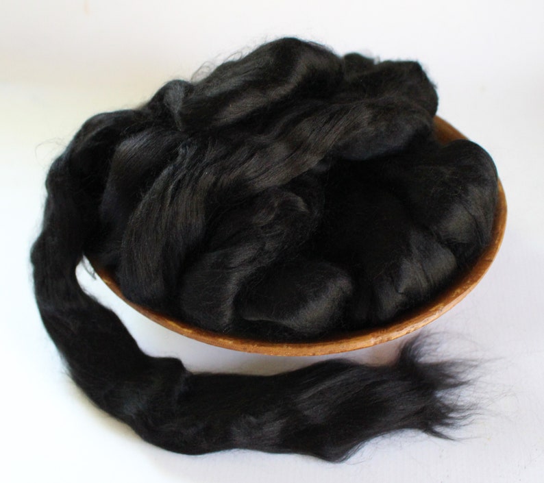 May include: A bowl filled with black alpaca fiber. The fiber is soft and fluffy, and it is perfect for spinning or felting.
