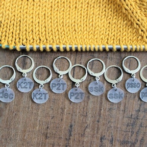 May include: Eight clear plastic stitch markers with metal rings. The markers are labeled with knitting abbreviations: dec, K2T, P2T, ssk, psso.