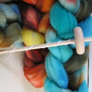 May include: A wooden spinning wheel with a white string wrapped around it. The wheel is sitting on top of a pile of colorful yarn.