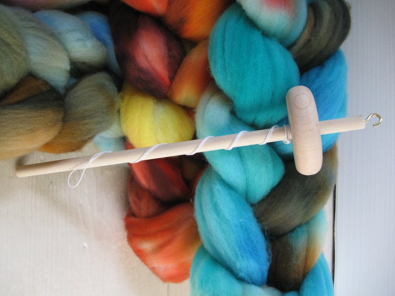 May include: A wooden spinning wheel with a white string wrapped around it. The wheel is sitting on top of a pile of colorful yarn.
