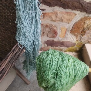 May include: Two skeins of yarn, one light blue and one green, are hanging from a wicker basket. The yarn is soft and fluffy, and it would be perfect for knitting or crocheting.