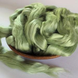Puede incluir: Un bol lleno de una gran cantidad de fibra de seda verde claro. La fibra es suave y esponjosa, y es perfecta para hilar o fieltro.