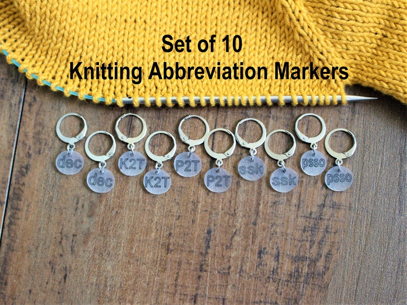 May include: Set of 10 knitting abbreviation markers. The markers are silver with clear plastic discs that have knitting abbreviations printed on them. The abbreviations include: dec, K2T, P2T, ssk, psso.