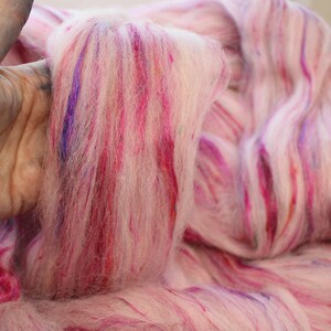 Puede incluir: Primer plano de un manojo de vell&oacute;n de lana rosa, blanco y morado. El vell&oacute;n est&aacute; te&ntilde;ido a mano con vetas de color.