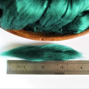 May include: A close-up of a teal green wool roving laid out next to a ruler. The roving is about 3 inches long.