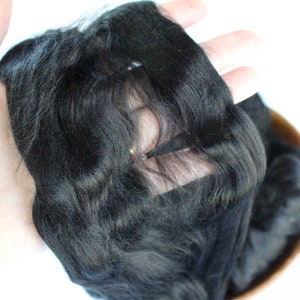 May include: A close-up of a black wig with a lace front. The wig is being held in a hand, and the lace front is visible.