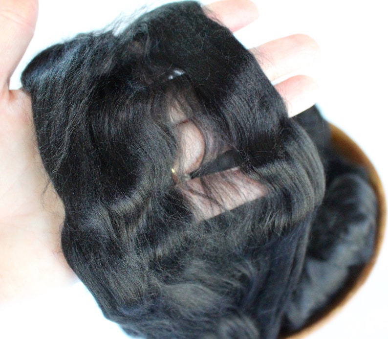 May include: A close-up of a black wig with a lace front. The wig is being held in a hand, and the lace front is visible.