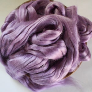 Peut inclure: Un tas de fibres douces de couleur lavande, peut-&ecirc;tre de la soie ou de la laine, remplit un panier rond et peu profond. Les fibres ont un &eacute;clat subtil, avec des reflets et des ombres qui cr&eacute;ent de la profondeur. La texture semble lisse et luxueuse, sugg&eacute;rant un mat&eacute;riau artisanal.