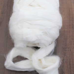 Puede incluir: Un gran paquete de fibra de algod&oacute;n blanco, perfecto para proyectos de artesan&iacute;a y relleno. El algod&oacute;n es suave y esponjoso, y se muestra sobre una superficie de madera.