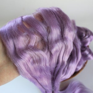 Peut inclure: Gros plan sur une poign&eacute;e de fibres de couleur lavande. La fibre a une texture douce et ondul&eacute;e, ressemblant &agrave; de la soie ou &agrave; un mat&eacute;riau similaire. La couleur est un m&eacute;lange de violets clairs et fonc&eacute;s, cr&eacute;ant un effet de d&eacute;grad&eacute; subtil. La fibre est tenue dans une main.