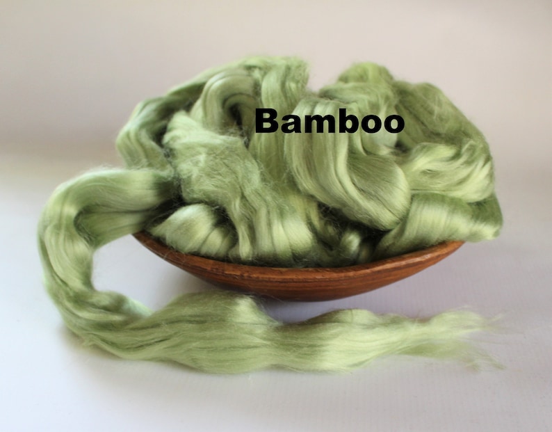 Puede incluir: Un bol lleno de fibra de bamb&uacute; verde claro, con un largo hilo de fibra que se extiende fuera del bol. La palabra "Bamb&uacute;" est&aacute; escrita en negro sobre la fibra.