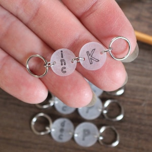 May include: A set of clear plastic stitch markers with silver rings. The markers are labelled with the letters "K" and "inc".