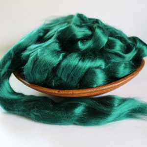 May include: A large amount of emerald green silk fiber in a wooden bowl. The fiber is soft and fluffy, and it is perfect for spinning or felting.