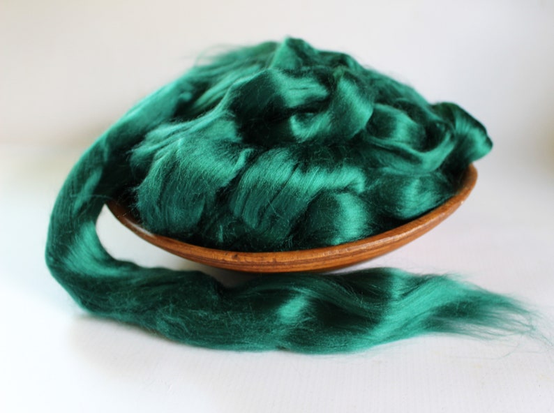 May include: A large amount of emerald green silk fiber in a wooden bowl. The fiber is soft and fluffy, and it is perfect for spinning or felting.