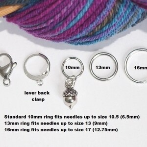May include: Four silver knitting stitch markers with acorn charms. The markers are in three sizes: 10 mm, 13 mm, and 16 mm. The text on the image reads: "Standard 10mm ring fits needles up to size 10.5 (6.5mm) 13mm ring fits needles up to size 13 (9mm) 16mm ring fits needles up to size 17 (12.75mm)"