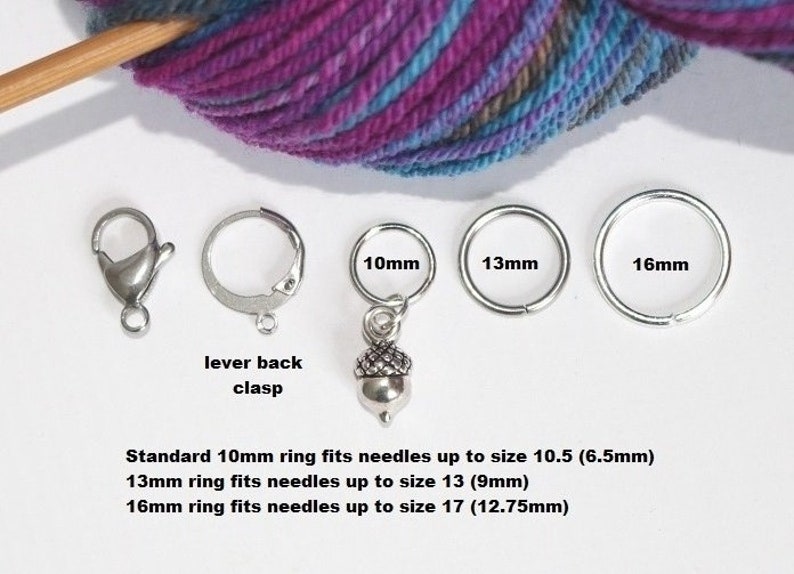May include: Four silver knitting stitch markers with acorn charms. The markers are in three sizes: 10 mm, 13 mm, and 16 mm. The text on the image reads: "Standard 10mm ring fits needles up to size 10.5 (6.5mm) 13mm ring fits needles up to size 13 (9mm) 16mm ring fits needles up to size 17 (12.75mm)"