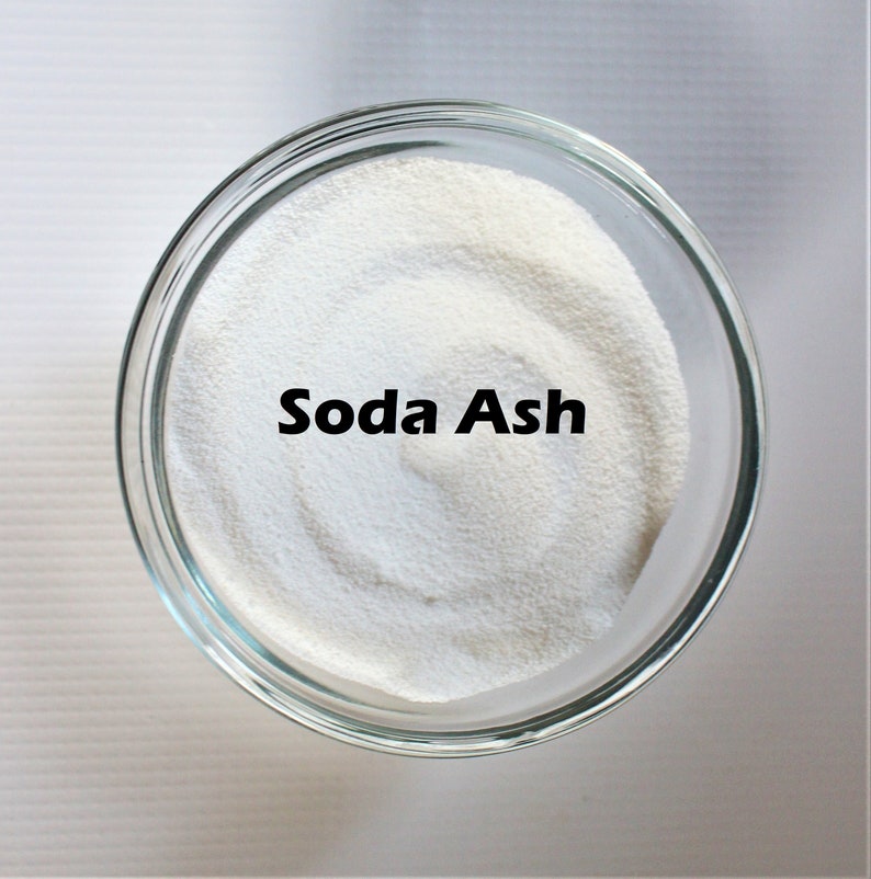 May include: A clear glass bowl filled with white soda ash powder. The words "Soda Ash" are printed in black on the powder.