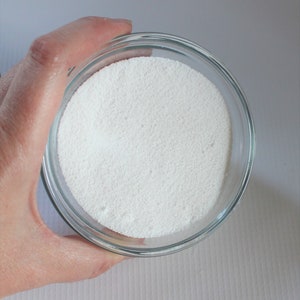 May include: A clear glass bowl filled with white powder. The bowl is being held by a hand.