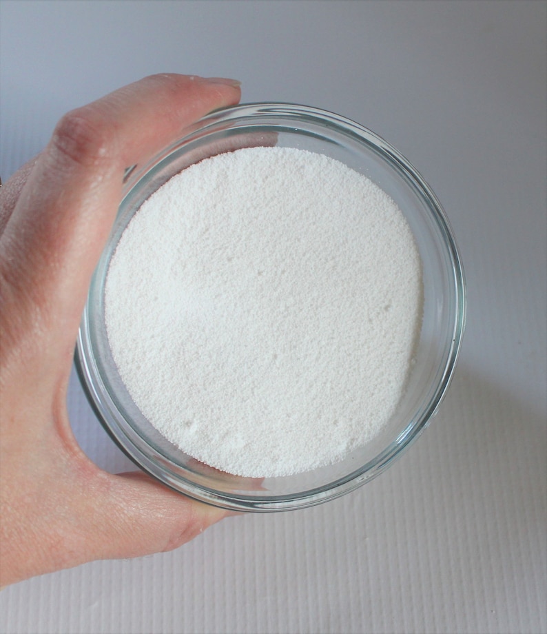 May include: A clear glass bowl filled with white powder. The bowl is being held by a hand.