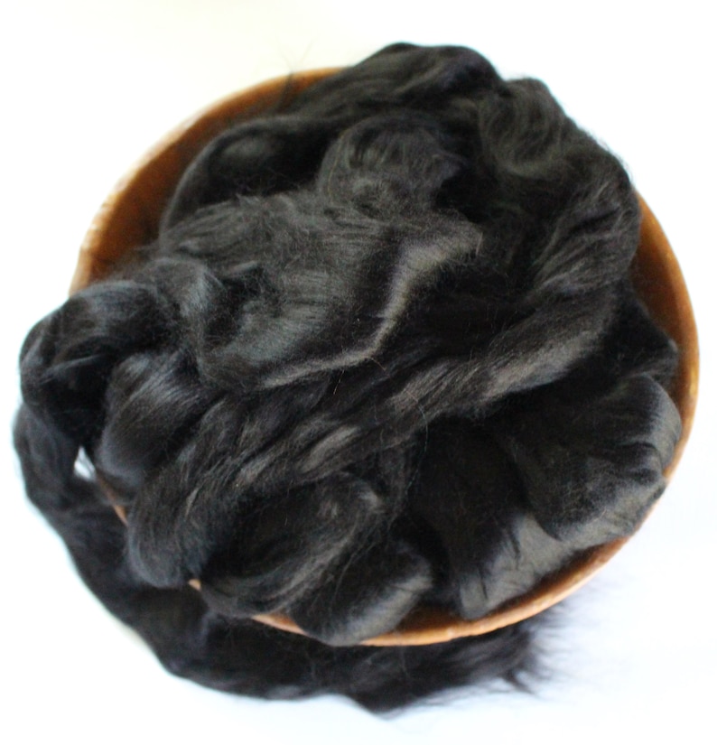 May include: A bowl filled with black silk fibers. The fibers are soft and fluffy, and they are perfect for spinning or felting.