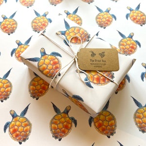 Peut inclure: Un cadeau emballé dans du papier blanc orné d'un motif répété de tortues de mer aquarelles orange, jaune et bleu. Le paquet est ficelé et comprend une étiquette marron avec le texte "The Print Bee".