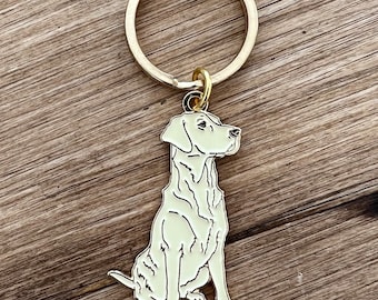 May include: A gold-colored metal keychain with a dog-shaped pendant. The pendant is a light green color with black outline details. The dog is sitting upright. The keychain ring is large and round.