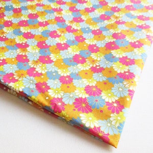 May include: A folded piece of fabric with a repeating floral pattern. The flowers are in shades of pink, yellow, blue, and white, set against a golden-yellow background. The fabric appears to be cotton or a similar material.