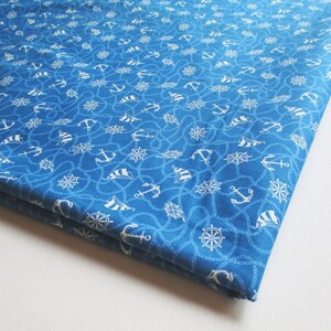 Op de afbeelding: Blauwe stof met een wit nautisch patroon van ankers, schepen en stuurwielen. De stof is dubbelgevouwen.