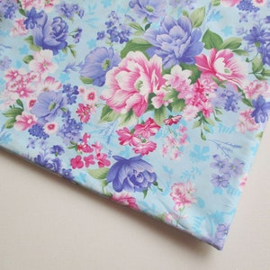 Puede incluir: Una tela azul claro con un patrón floral. Las flores son rosas, moradas y blancas. La tela tiene un tacto suave y delicado.