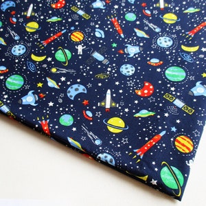 Puede incluir: Tela azul marino con un patrón repetido de planetas, estrellas, cohetes y naves espaciales de colores.