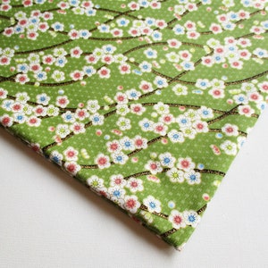以下が含まれることがあります： 白、ピンク、青の花柄の緑色の生地。生地は、枝に小さな花が繰り返し描かれたデザインです。