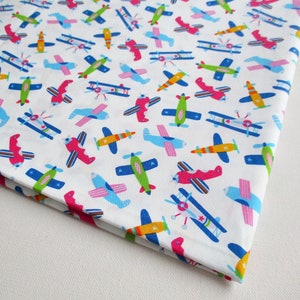 Pode incluir: Tecido branco com um padrão repetido de aviões coloridos. Os aviões são de vários estilos e cores, incluindo azul, vermelho, verde, amarelo e rosa.