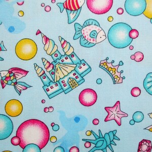Puede incluir: Una tela azul con un patrón repetitivo de ilustraciones coloridas con temática marina. El patrón incluye un castillo, peces, conchas marinas, estrellas de mar, burbujas y una corona.