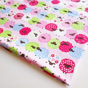 May include: Pink fabric with a repeating pattern of colourful sheep. The sheep are in various colours, including pink, green, blue, and white. Each sheep has a brown face and black eyes.
